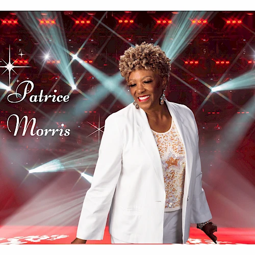 A smiling woman in a white blazer on a stage with bright lights; text reads “Patrice Morris” in cursive on the left.