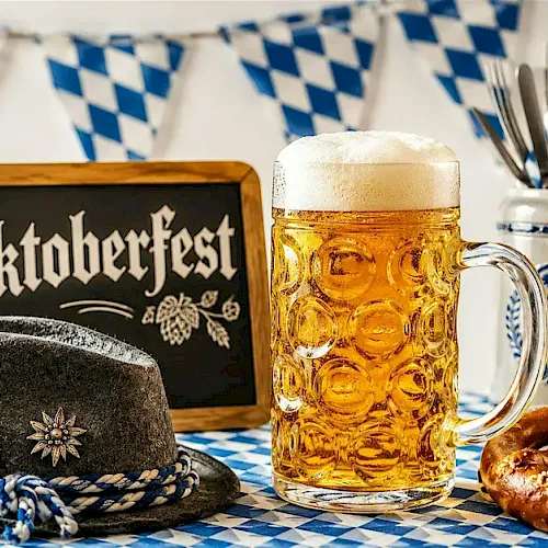 Oktoberfest scene with a beer stein, Bavarian hat, pretzel, and blue-and-white table decorations.