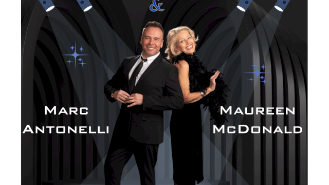 Two people in formal attire pose on a stage under spotlights, with names “Marc Antonelli” and “Maureen McDonald” displayed; a decorative backdrop.