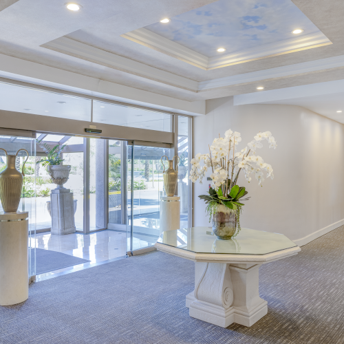 A bright, modern living space with large glass doors to a patio, a beige sofa, and a white floral arrangement under recessed ceiling lights.