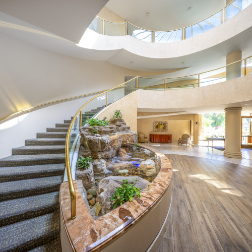 A modern, bright interior with curved staircase, warm wood accents, and a welcoming lounge area featuring plants and soft lighting.