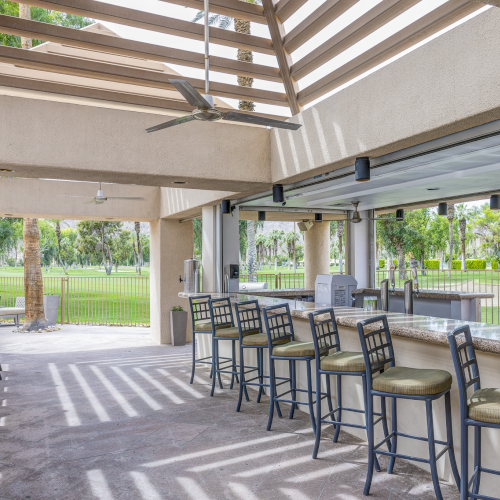 A bright outdoor dining area with a covered pergola, string lights, wicker furniture, and a view of a lush, sunny yard.