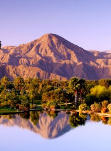 A tranquil lake reflecting autumn trees and colorful hills under a clear sky.
