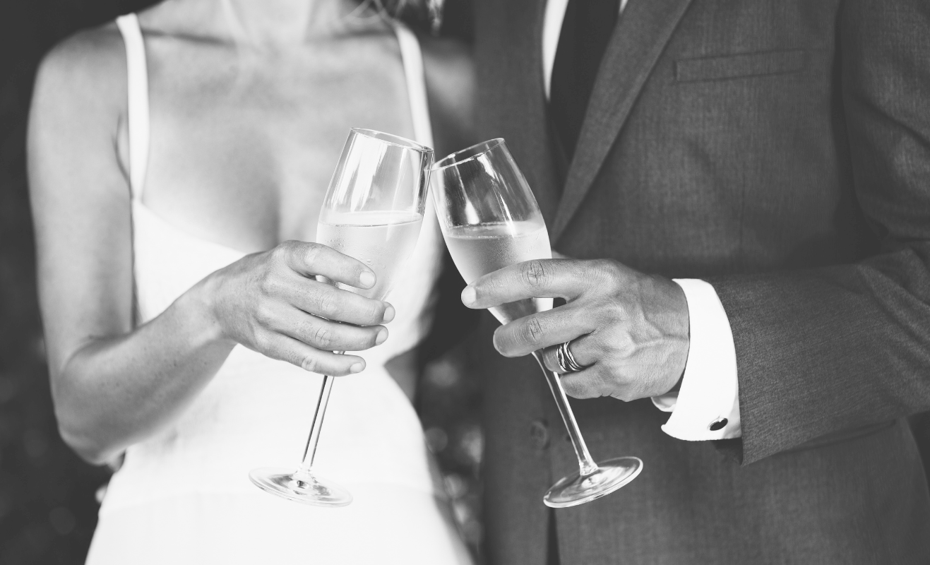 A couple toasting with champagne flutes at a wedding; their attire suggests a formal celebration.