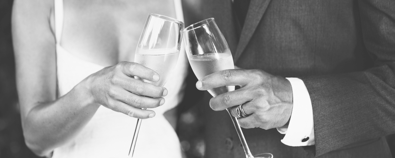 A couple toasting with champagne flutes at a wedding; their attire suggests a formal celebration.