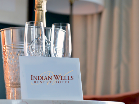 A drink setup with metal ice bucket and empty champagne flutes on a table, branded &ldquo;Indian Wells Resort & Hotel&rdquo; card in the foreground.