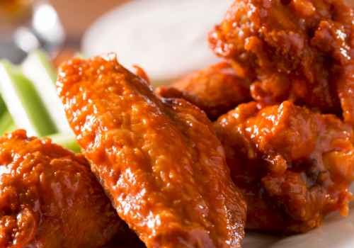 Crispy-looking glazed chicken wings on a plate with celery sticks in the background. delicious and saucy wings served hot.
