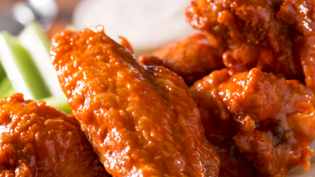 Crispy-looking glazed chicken wings on a plate with celery sticks in the background. delicious and saucy wings served hot.