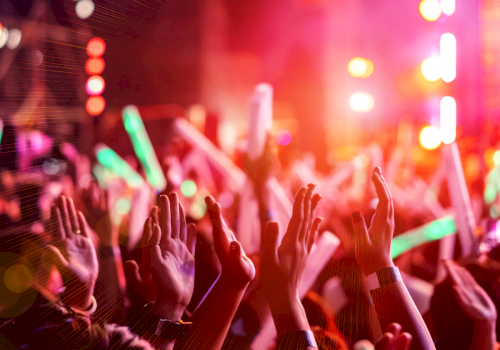 A crowded concert scene with hands raised, colorful stage lights, and a vibrant, energetic atmosphere at night.