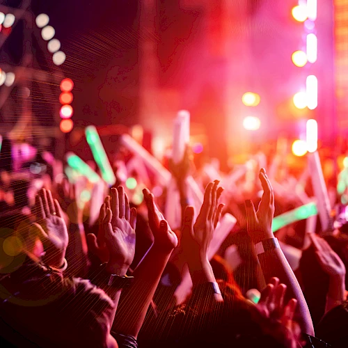 A crowded concert scene with hands raised, colorful stage lights, and a vibrant, energetic atmosphere at night.