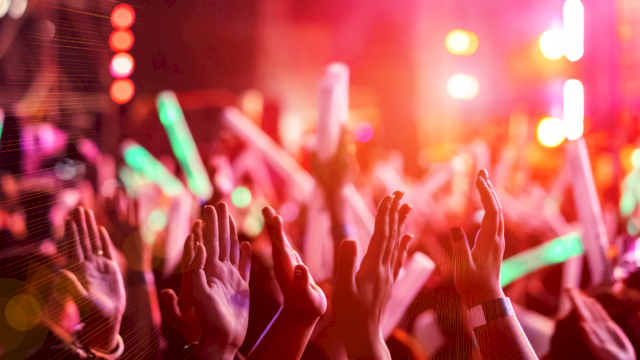 A crowded concert scene with hands raised, colorful stage lights, and a vibrant, energetic atmosphere at night.