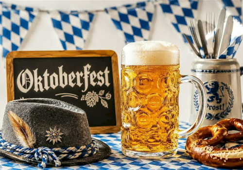 Oktoberfest scene with a beer stein, Bavarian hat, pretzel, and blue-and-white table decorations.